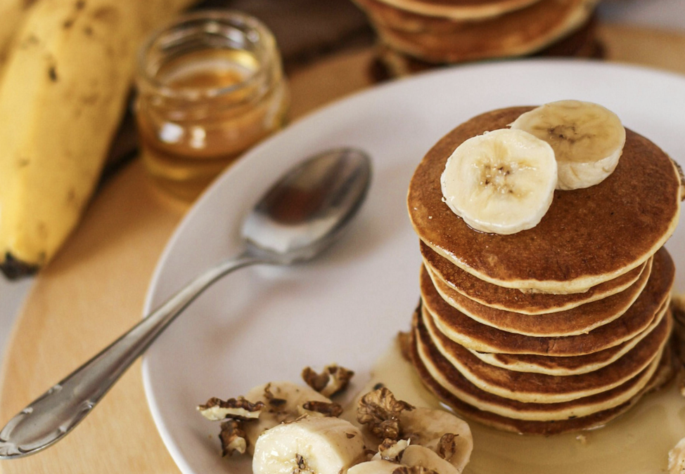 A stack of pancakes topped with banana slices and drizzled with syrup on a plate.